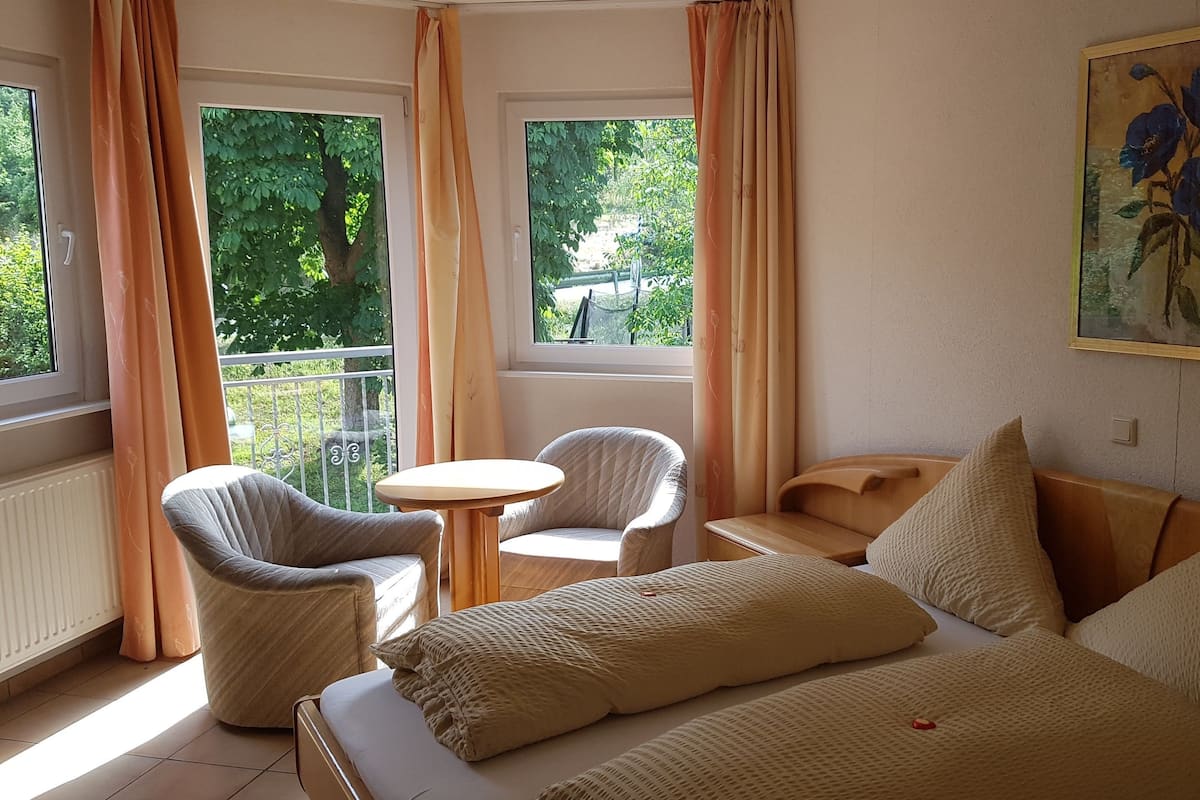 A hotel room with a bed, two chairs, a small table, and a painting on the wall.