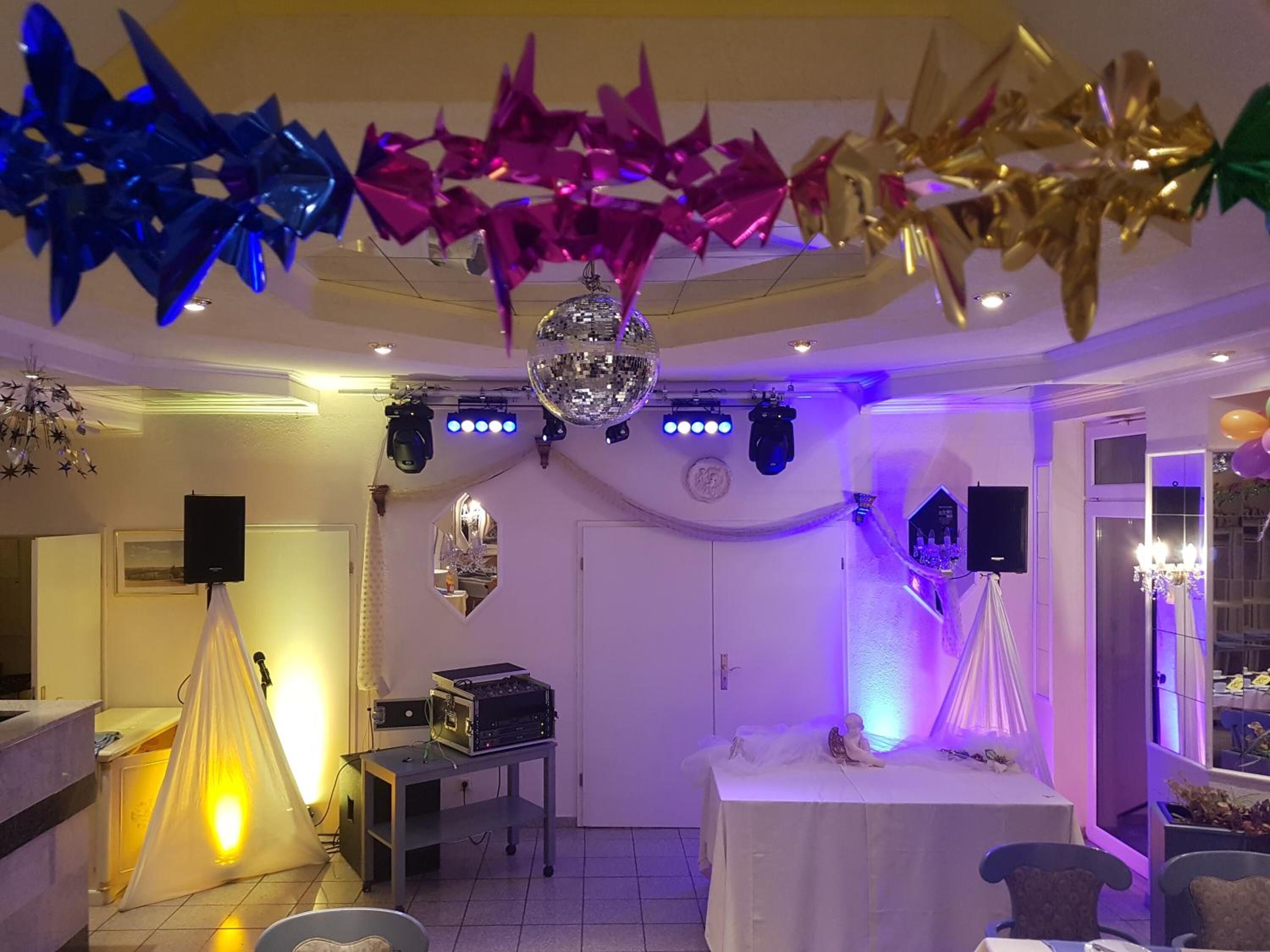 A room with a disco ball, stage lighting, and decorative elements like balloons and streamers.