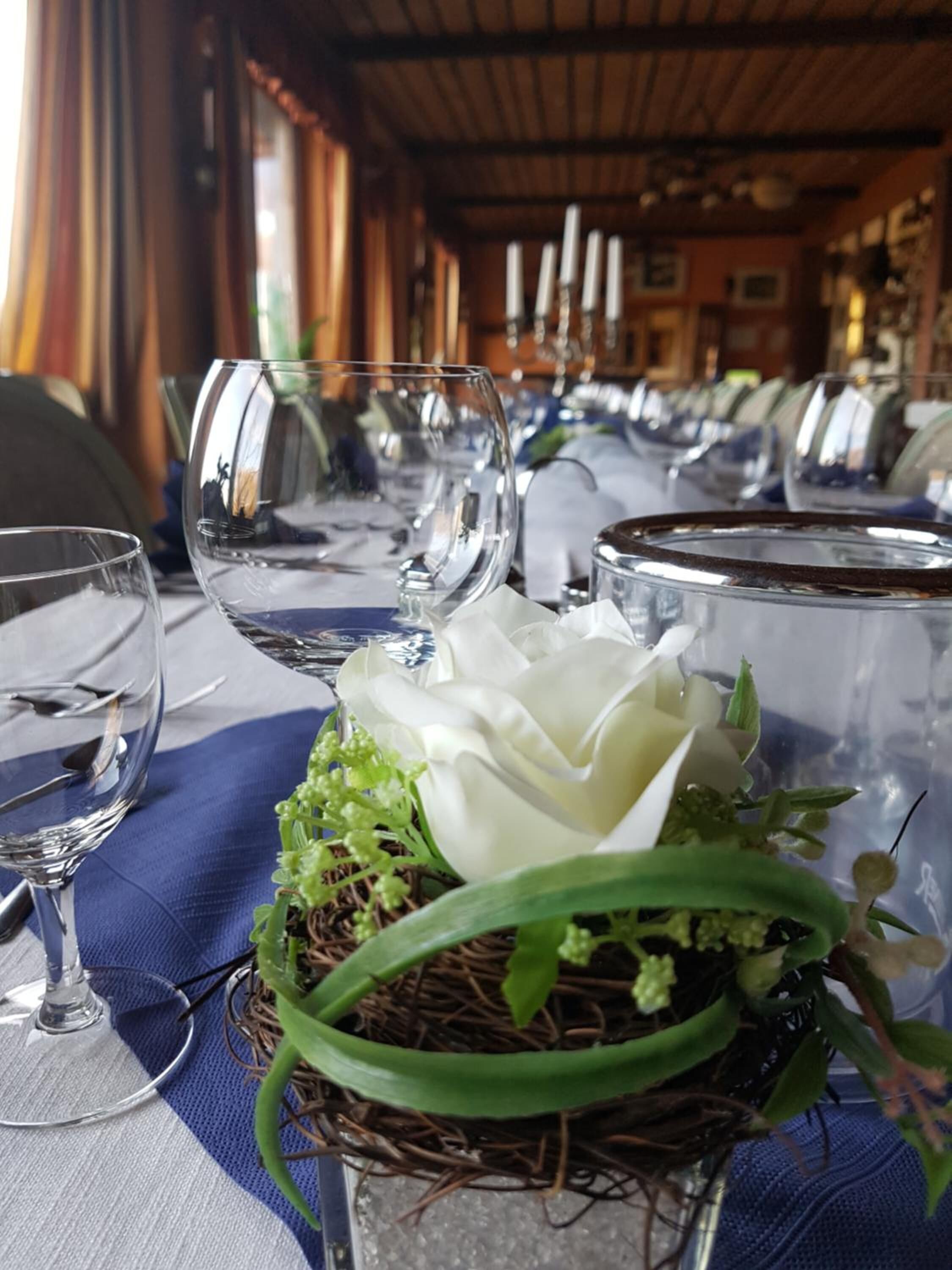 A dining table with empty wine glasses and a centerpiece of a white flower and greenery.