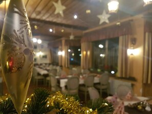 A restaurant interior with tables and chairs, star-shaped ceiling decorations, and a Christmas tree with lights.