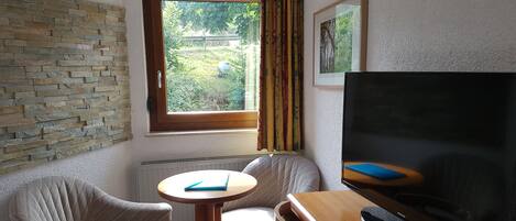 A room with a stone wall, a window with curtains, a television, and two chairs.