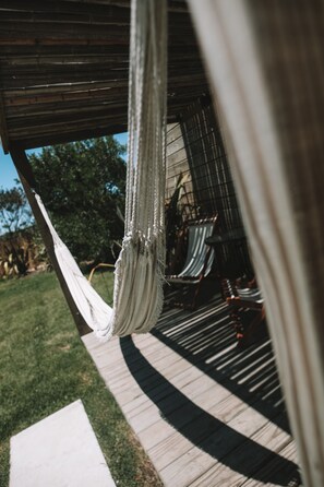 A hammock hanging from a wooden structure, a wooden deck, and a metal railing.