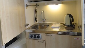A compact kitchen with a microwave, sink, kettle, and storage shelves. - 22 43 Clanricarde Gardens Studio (London)