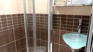 A bathroom with a glass shower enclosure, a white sink with a glass basin, and a tiled wall with a two-tone pattern. - 22 43 Clanricarde Gardens Studio (London)