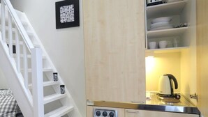 A compact kitchen with a built-in stove, a kettle, and shelves with dishes. - 22 43 Clanricarde Gardens Studio (London)
