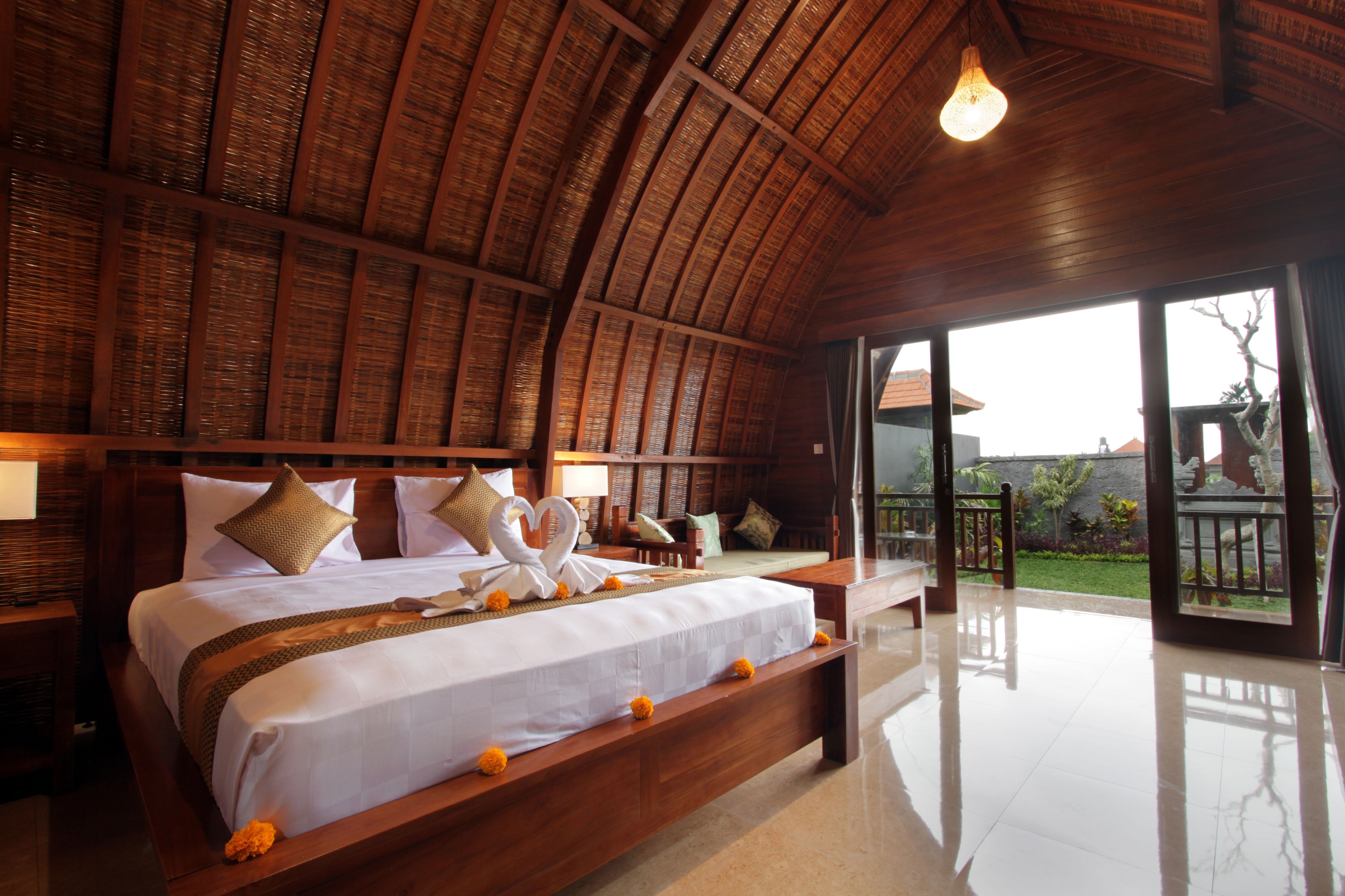 A spacious bedroom with a large bed, wooden headboard, and a view of the garden through a sliding glass door.