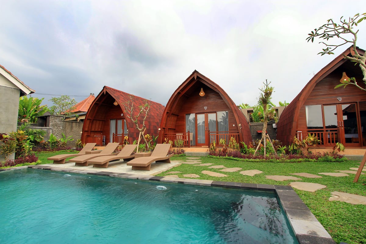 A pool area with lounge chairs and a wooden building with a triangular roof.