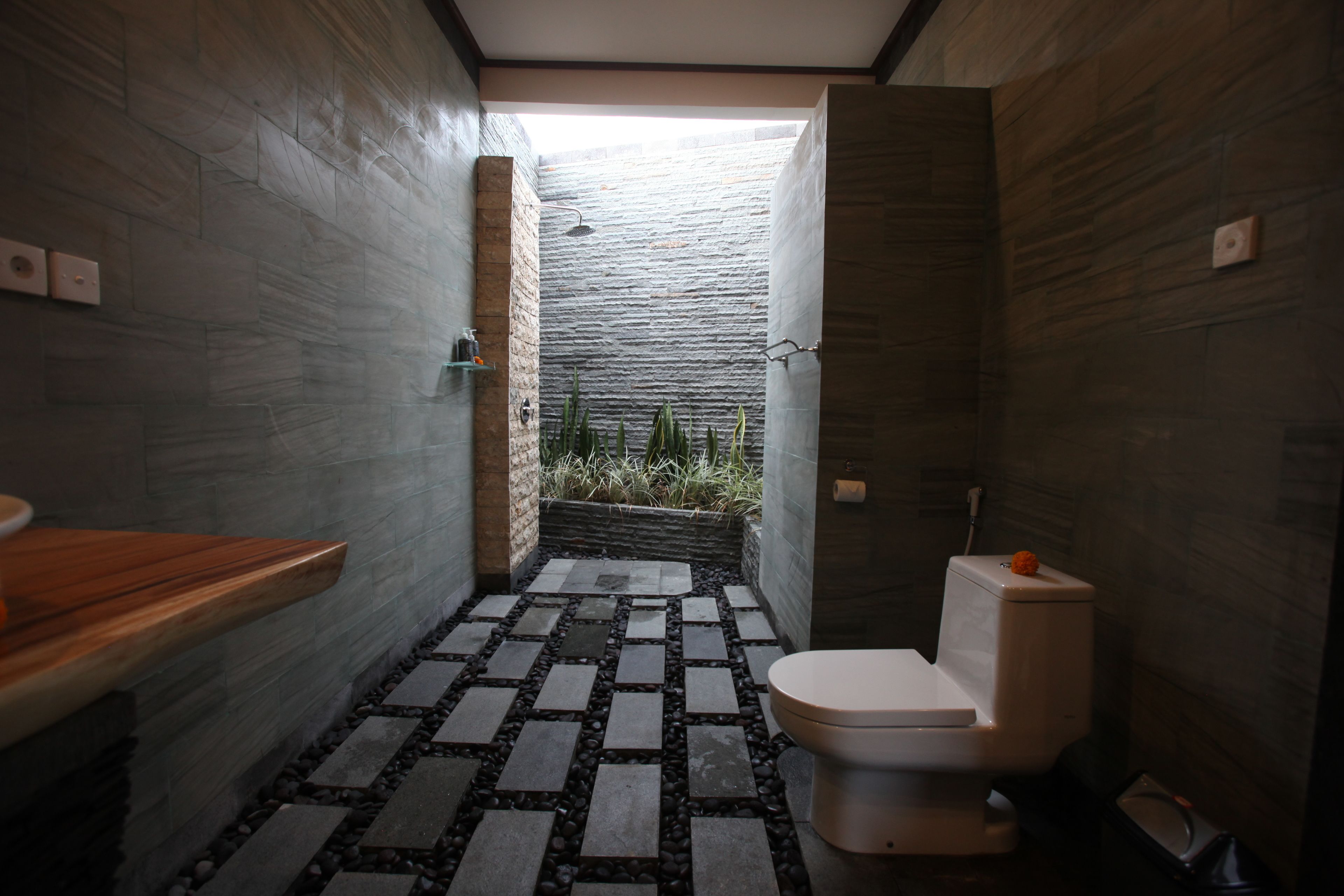 A modern bathroom with a stone-tiled floor, a wooden vanity, and a toilet.