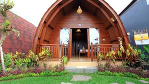 A wooden lodge with a pitched roof, a porch with railings, and a garden with various plants. - Pondok Naya (Ubud)