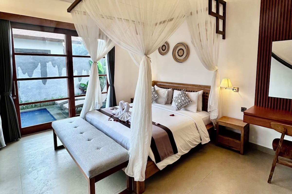 A four-poster canopy bed with a bench, bedside tables, and a view of the outdoors.