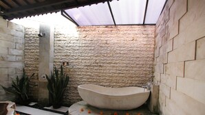 A stone-walled bathroom with a freestanding bathtub, a shower, and a small sink. - Pondok Naya (Ubud)