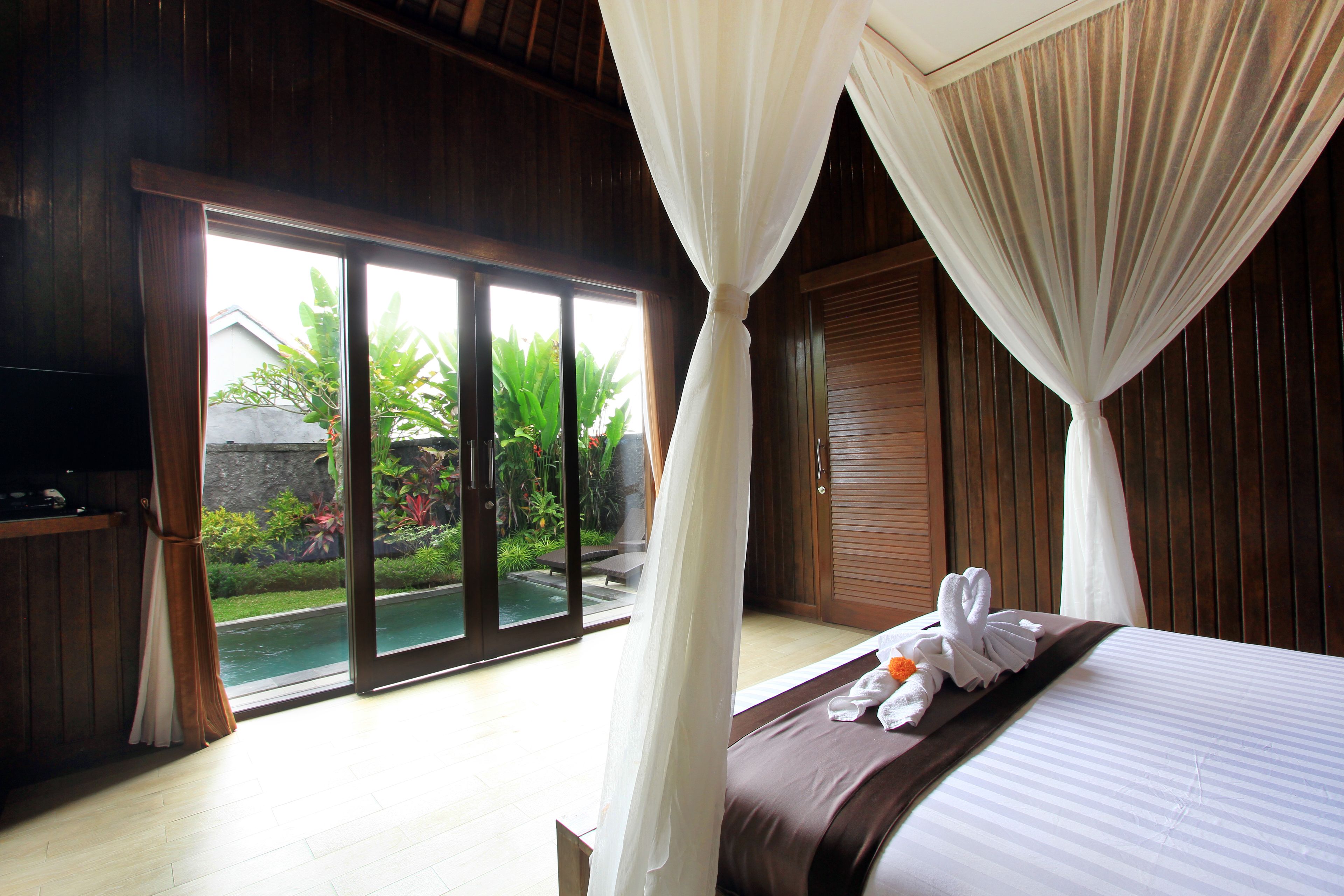 Ein Schlafzimmer mit Bett, Fernseher und einer Schiebetür zum Pool.