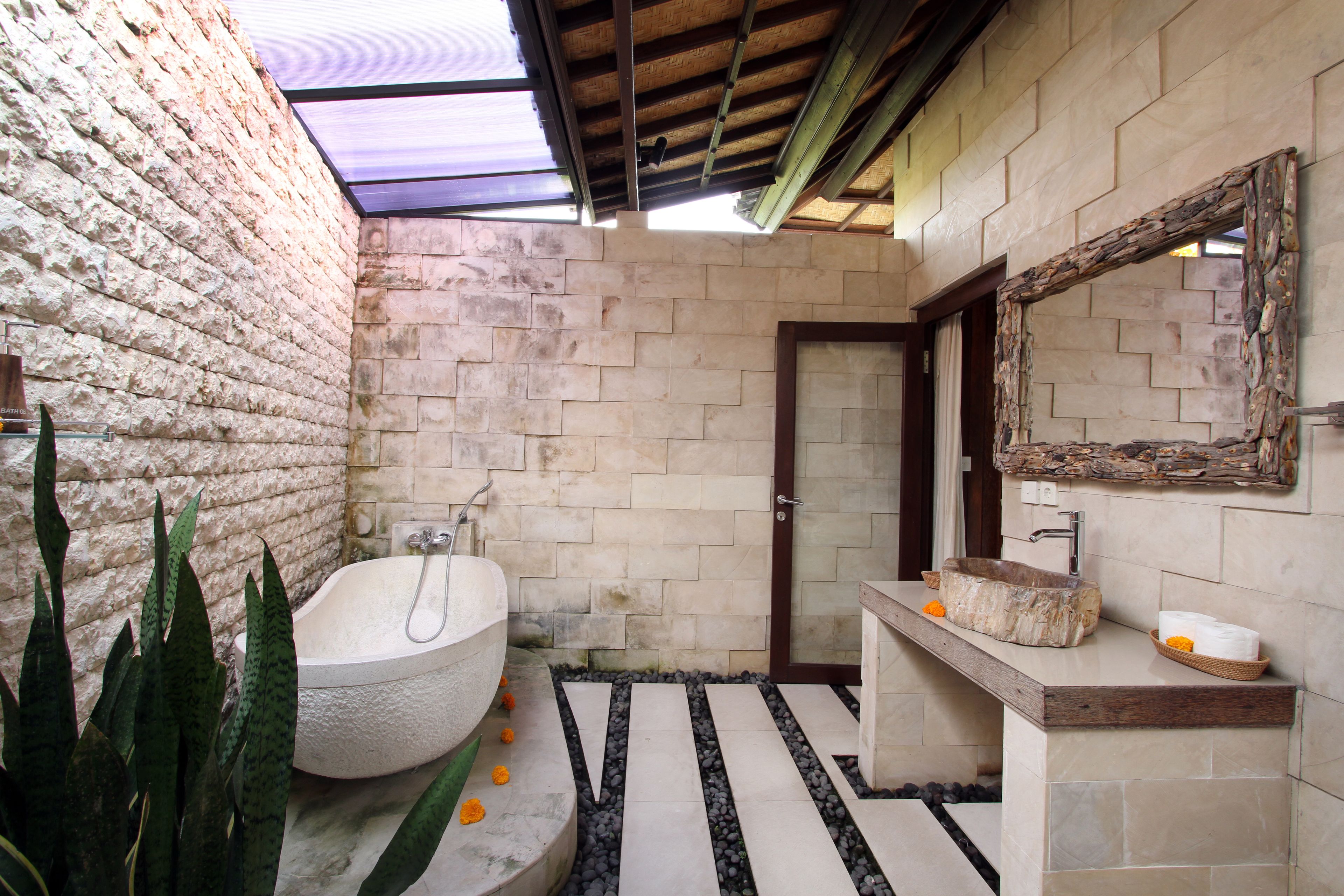 A bathroom with a stone bathtub, a wooden vanity, and a large mirror.