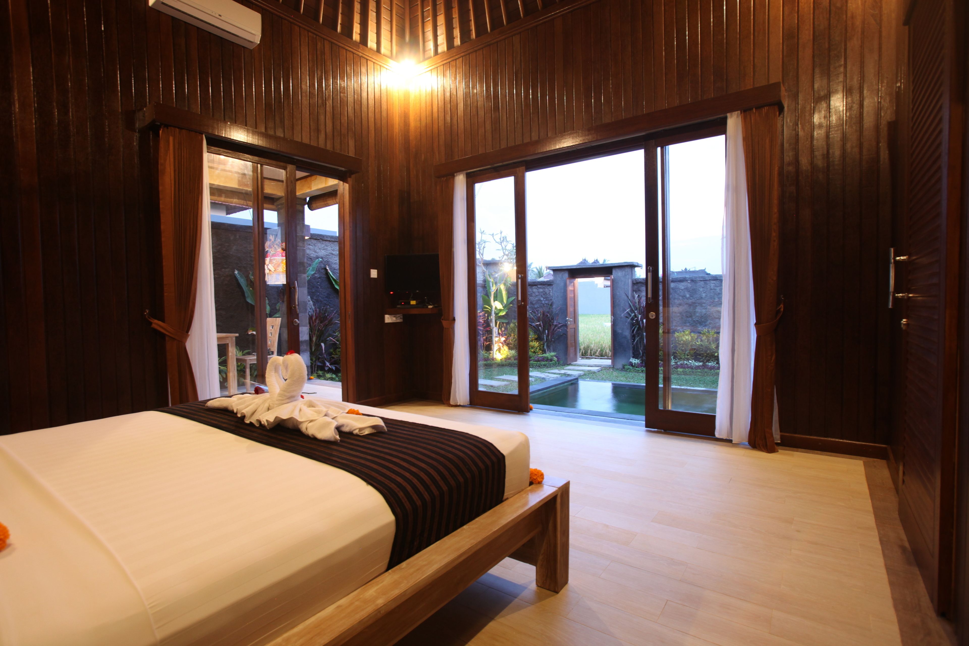 A hotel room with a large bed, wooden walls, and a sliding glass door leading to a garden.