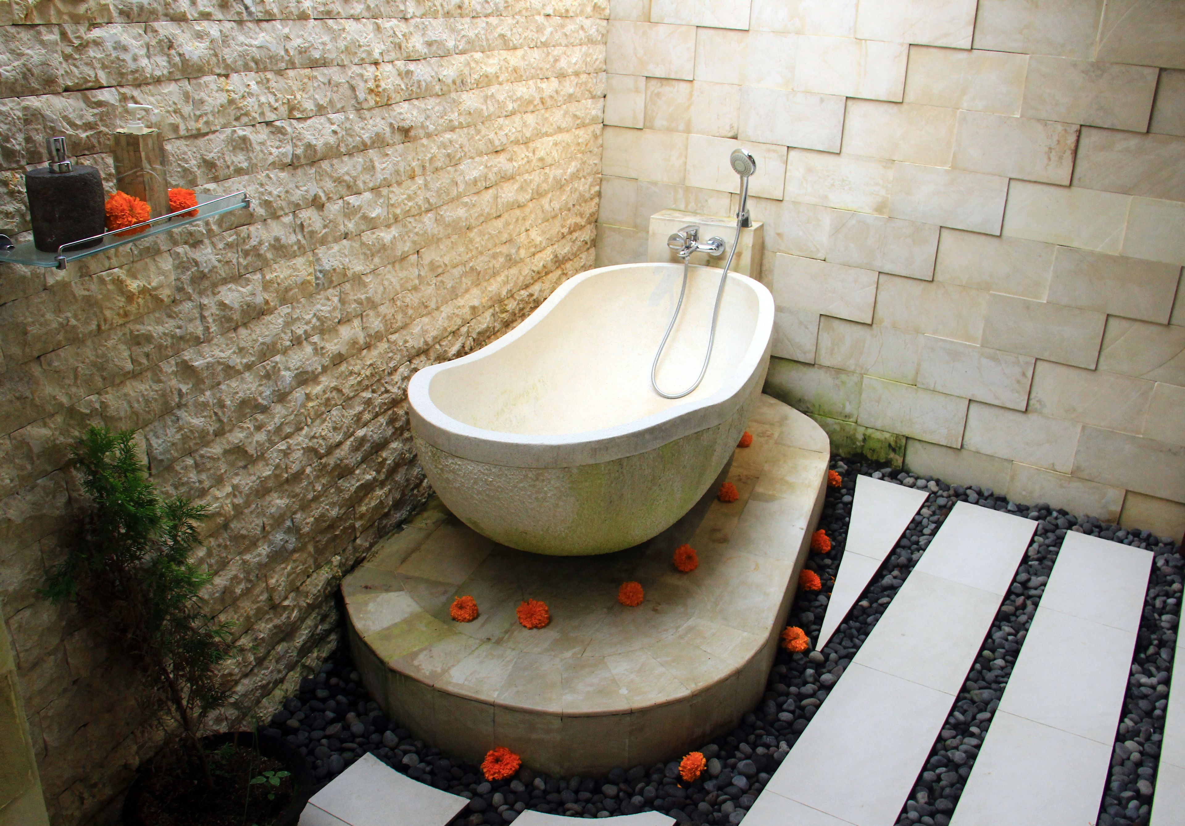 A stone bathtub in a corner with a stone wall and a small shelf with decorative items.