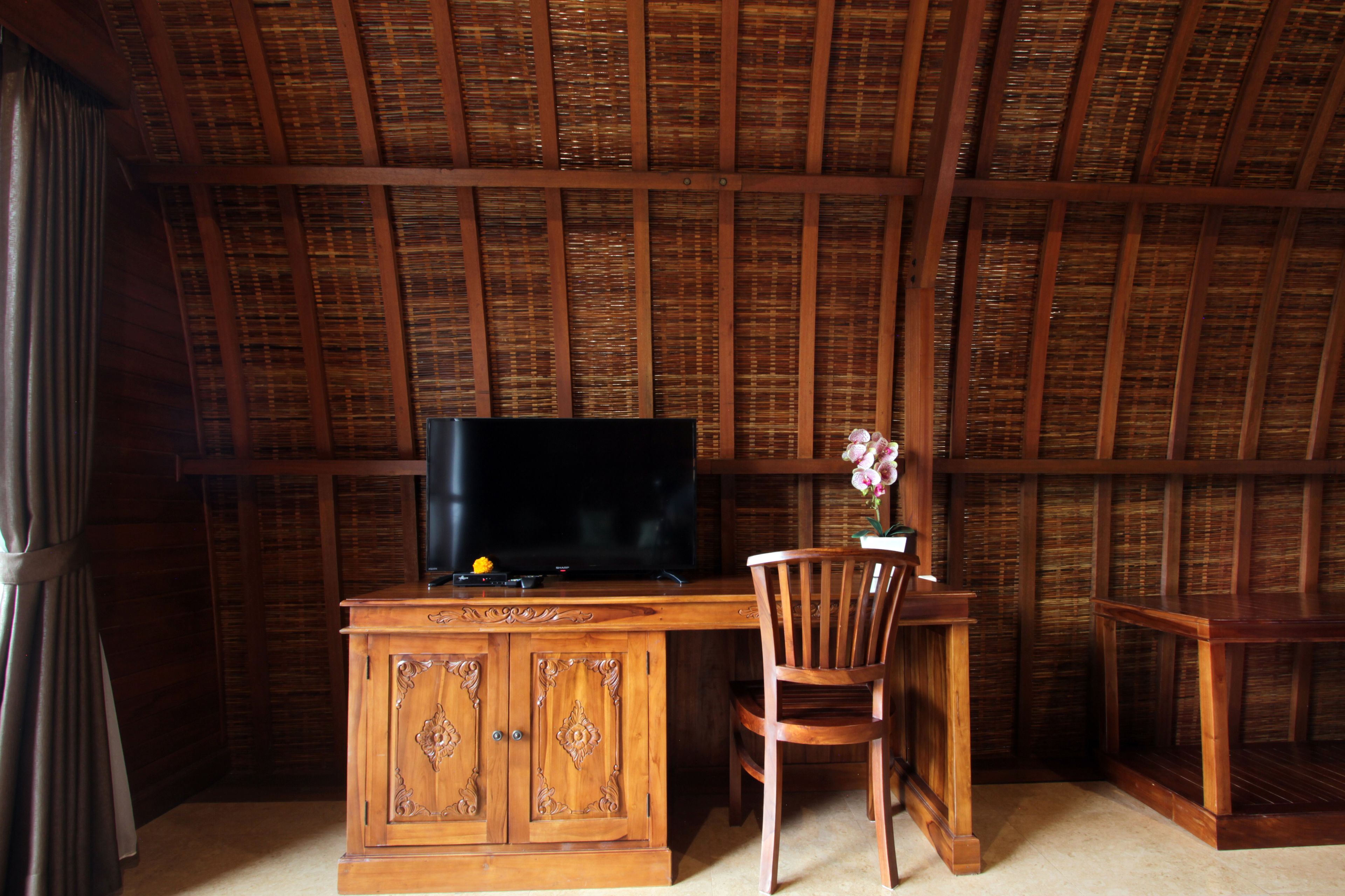 Un escritorio de madera con una televisión, una silla y una mesita con un jarrón de flores.