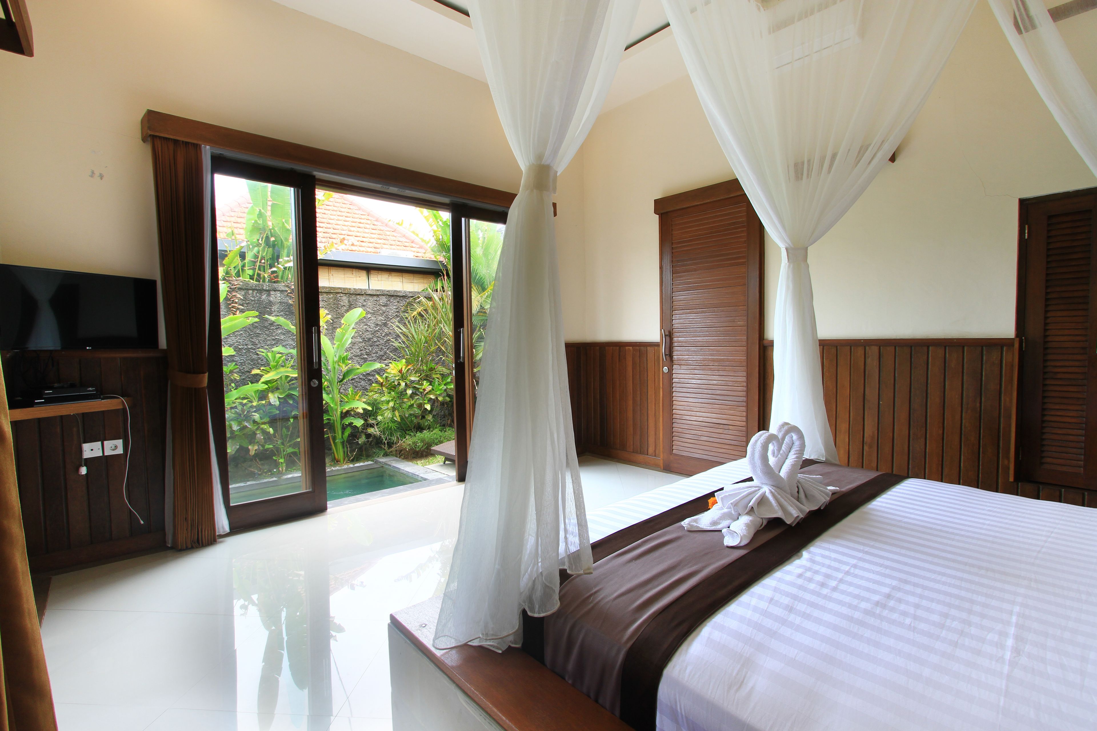 Habitación de hotel con cama, televisión y puerta corrediza de vidrio que da a una zona de piscina.