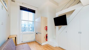 Une chambre moderne avec un plancher en bois, un canapé, une armoire, un téléviseur et une fenêtre avec des stores.