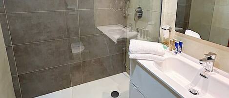 A modern bathroom with a glass-enclosed shower, a large mirror, and a white vanity with a sink.