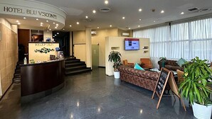Un hall d’hôtel comprenant un comptoir d’accueil, un escalier, un espace salon et une grande fenêtre.