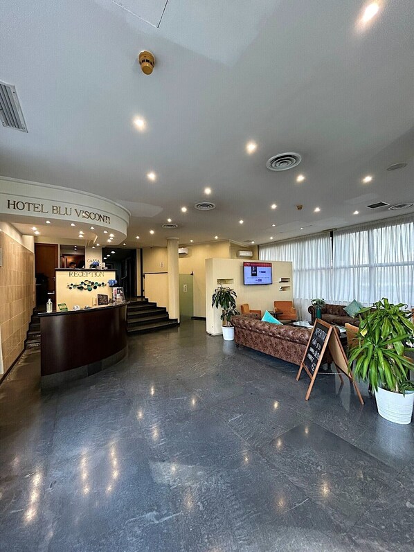 Un hall de hotel con una recepción, una escalera, un área de descanso y un ventanal grande.