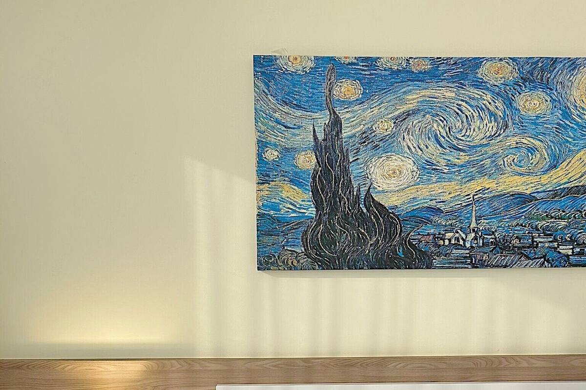 Une chambre d’hôtel avec un lit, une table de chevet avec une lampe, une prise de courant et un tableau représentant un ciel nocturne étoilé.