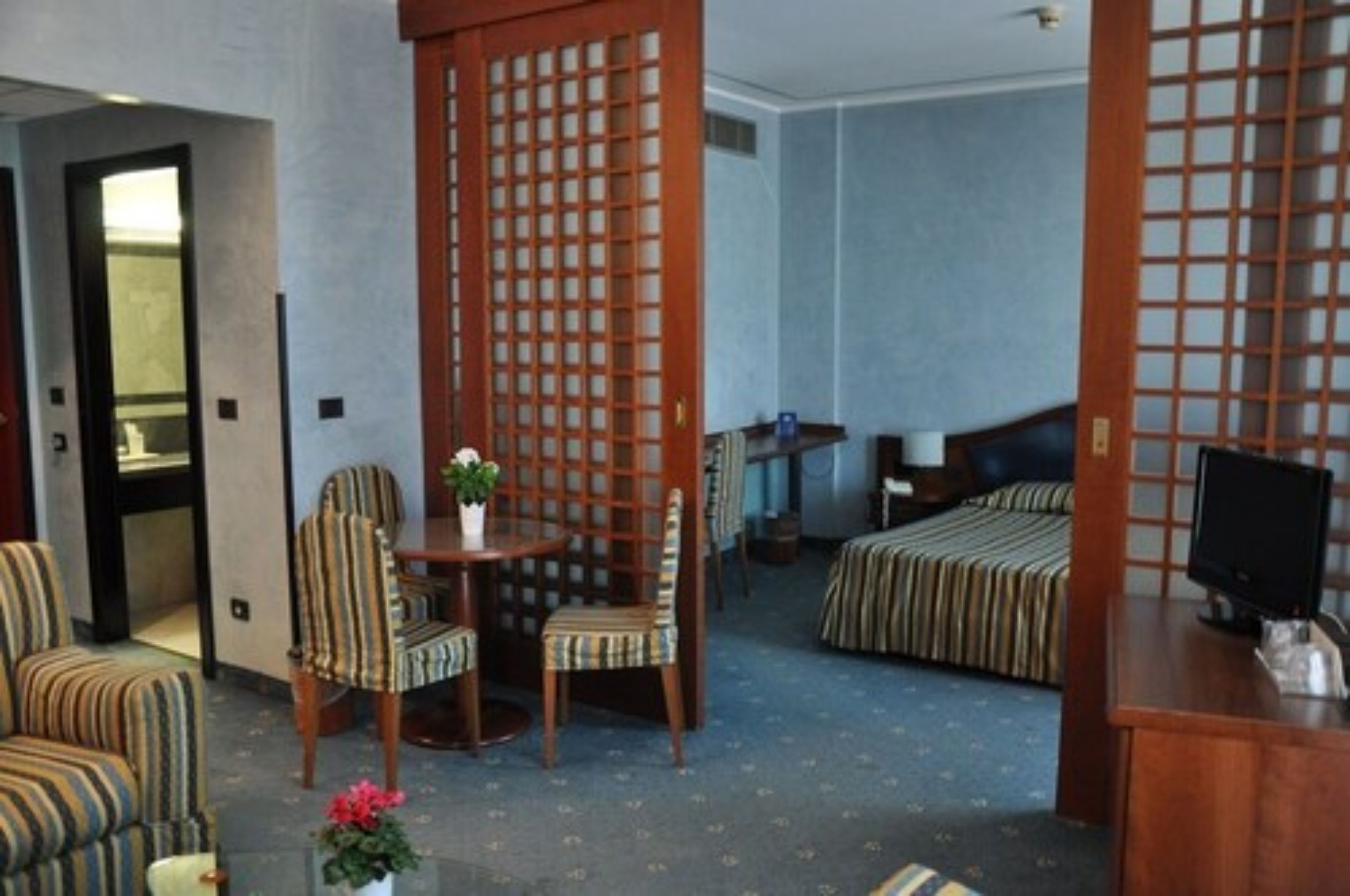 Una habitación de hotel con una cama, un escritorio con computadora, una silla y una mesita con una planta.