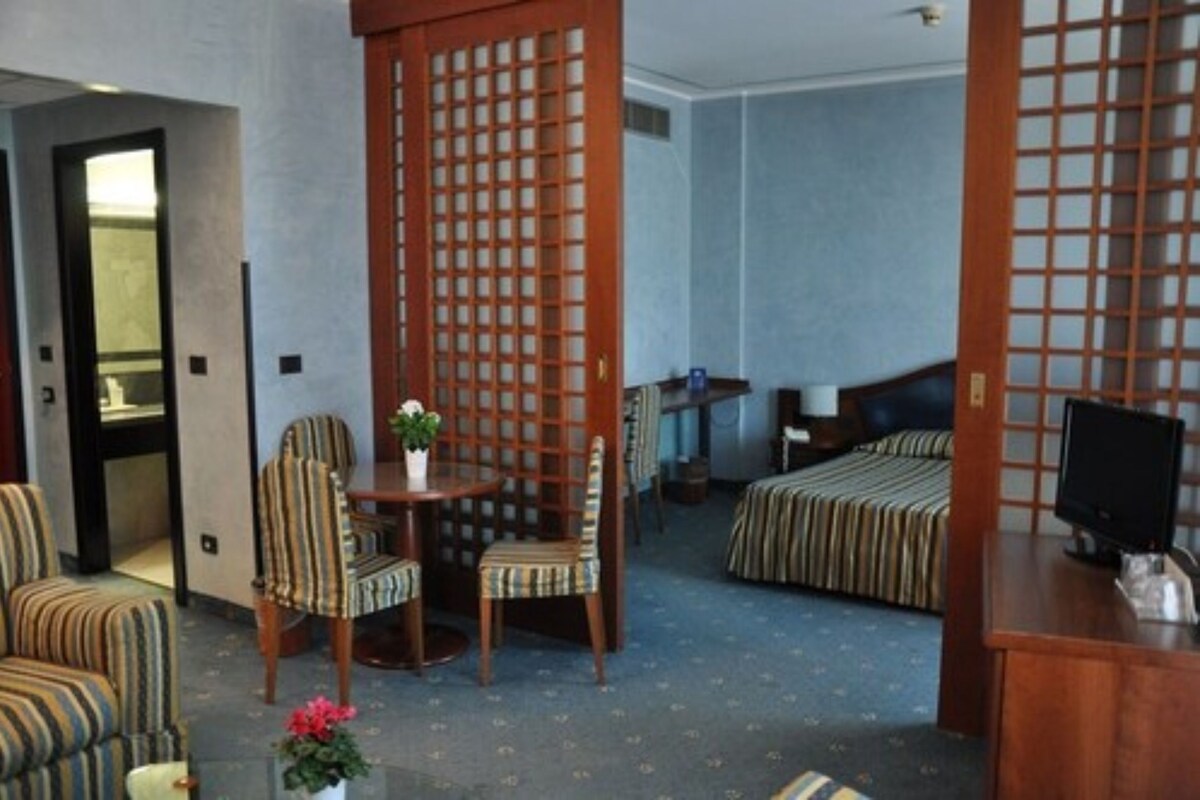 Una habitación de hotel con una cama, un escritorio con computadora, una silla y una mesita con una planta.