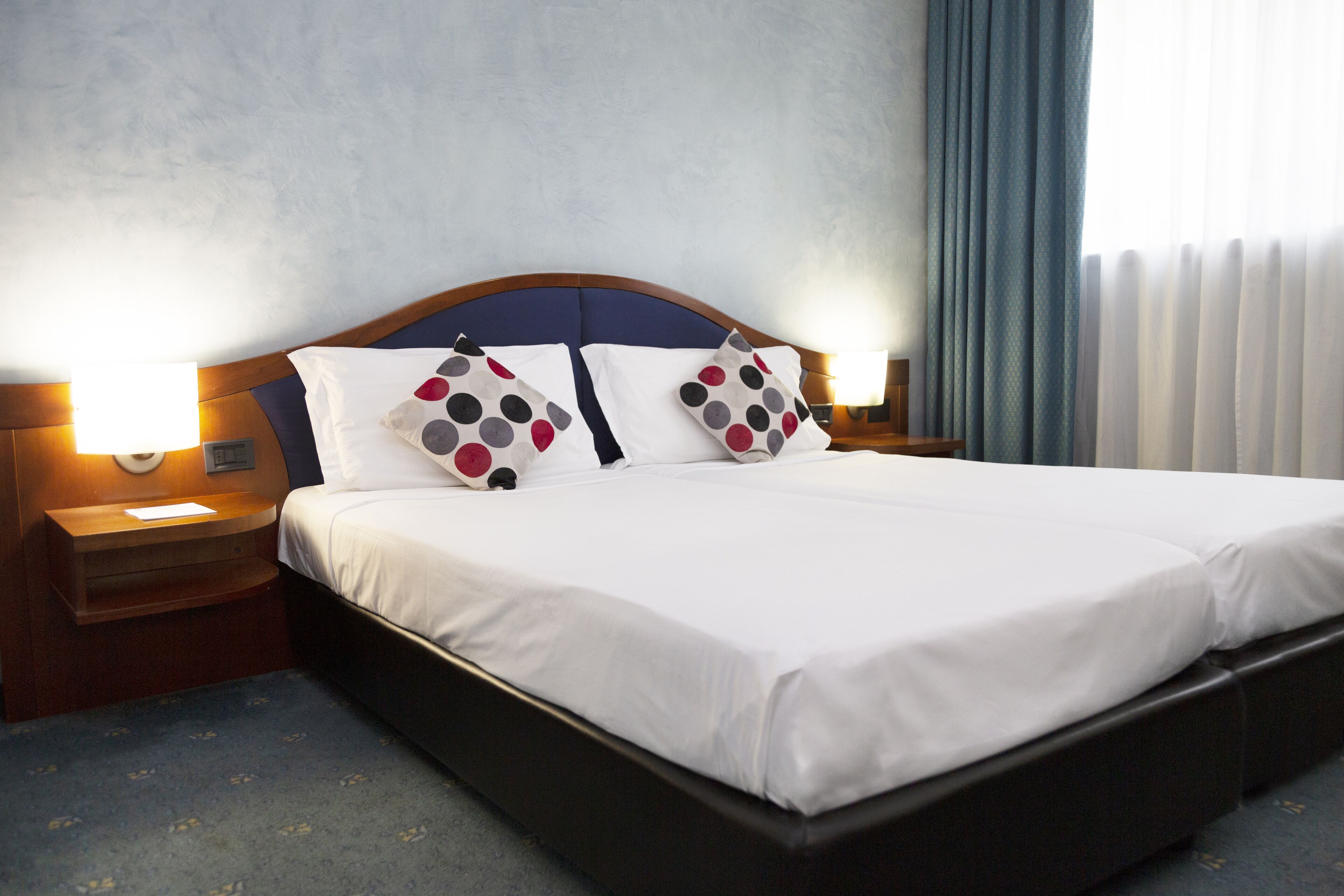 A hotel room with a large bed, two bedside tables with lamps, and a window with curtains.