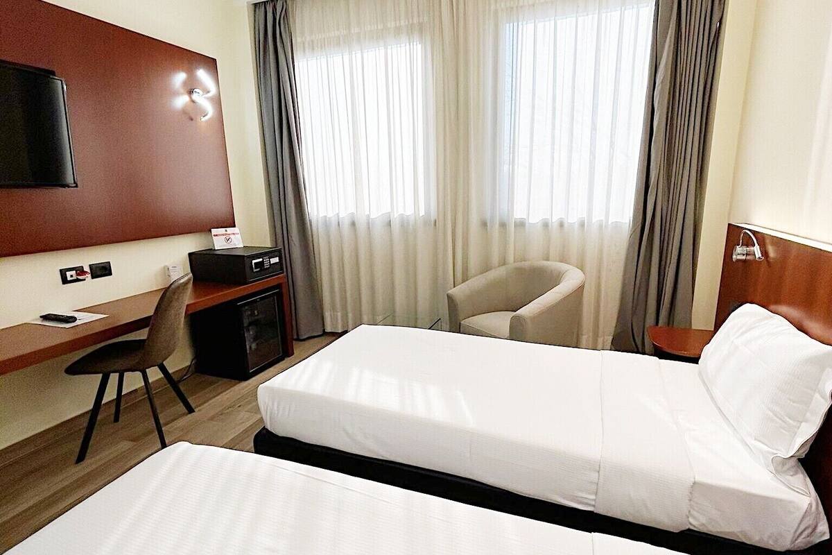 Une chambre d’hôtel avec deux lits, un bureau, une chaise, une télévision et des rideaux.