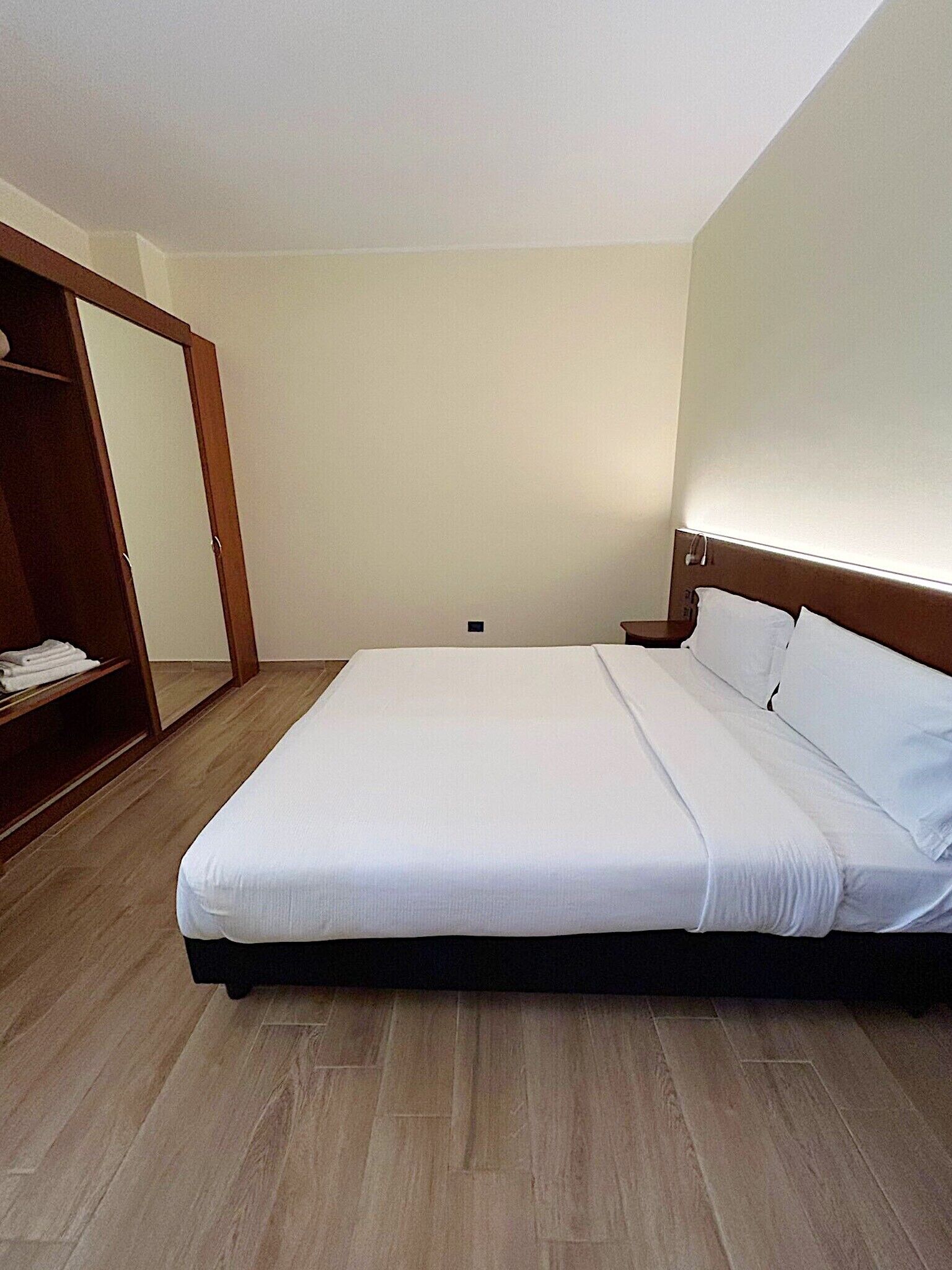 A bedroom with a bed, wooden wardrobe, and a mirror.