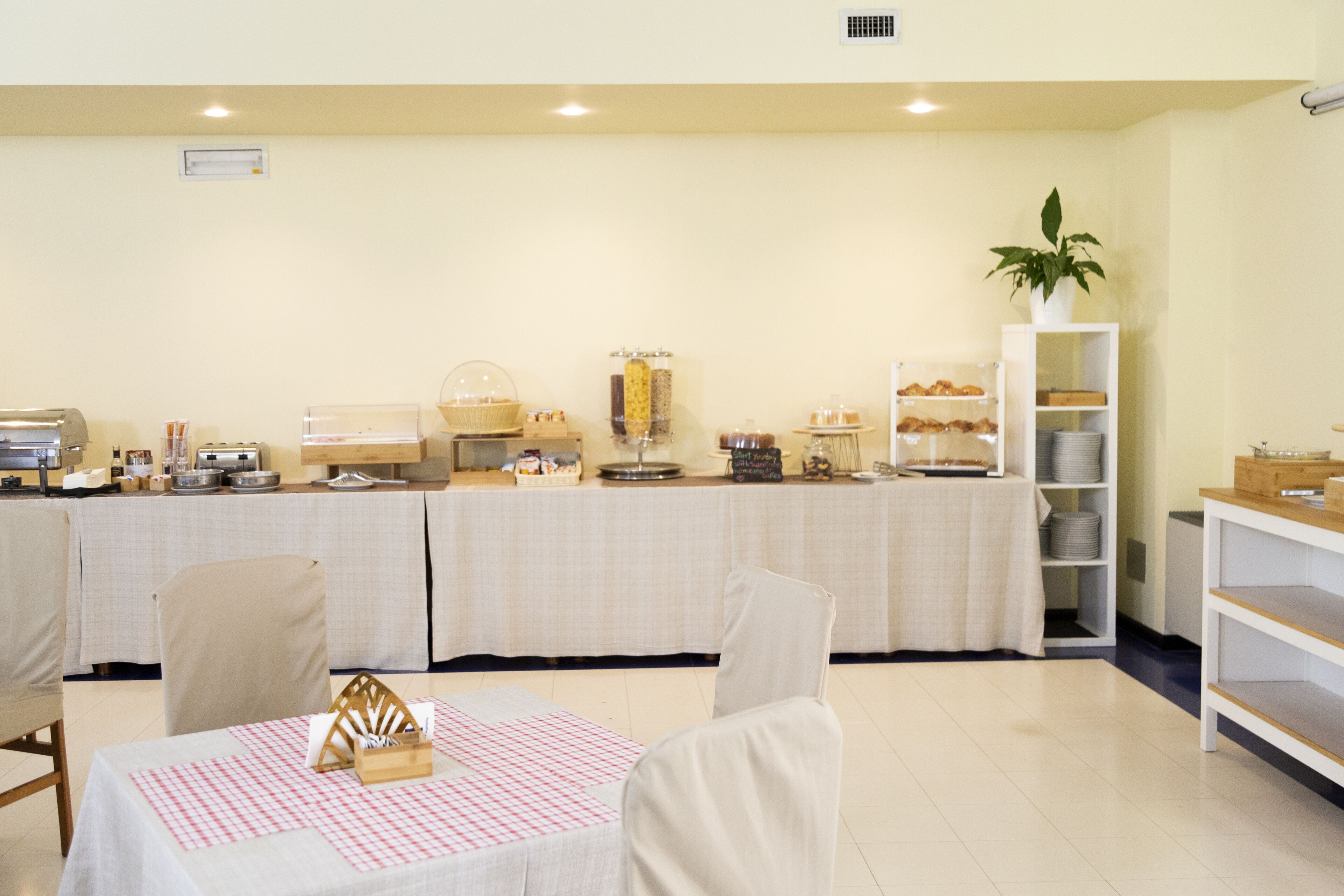 Zona de desayuno tipo buffet con una variedad de alimentos, una estación de café y una repisa con platos y tazones.