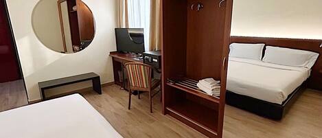 A hotel room with a large bed, a desk with a computer, a chair, a wardrobe, and a mirror.