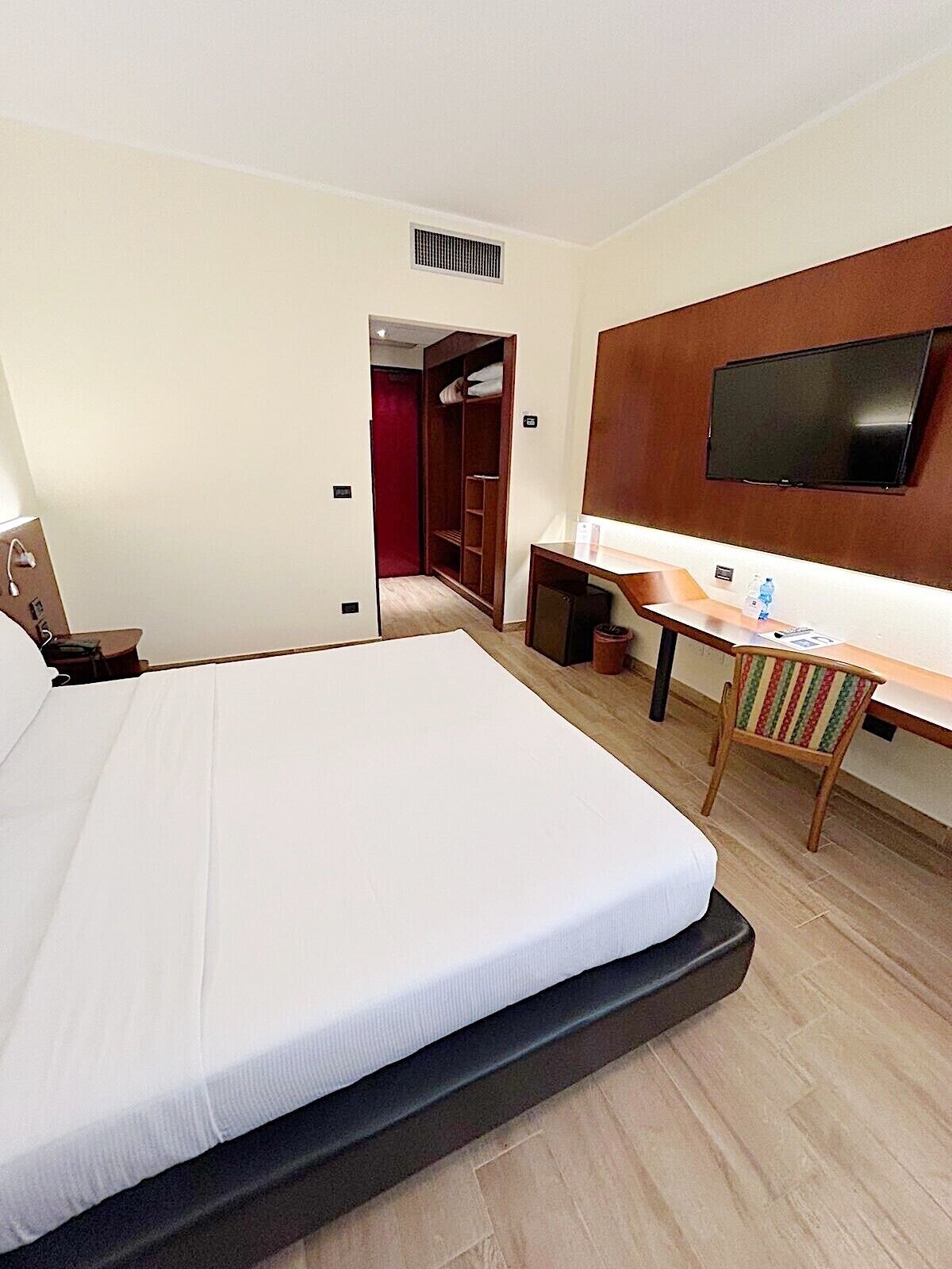 Habitación de hotel con una cama grande, un escritorio con silla, televisor y armario.