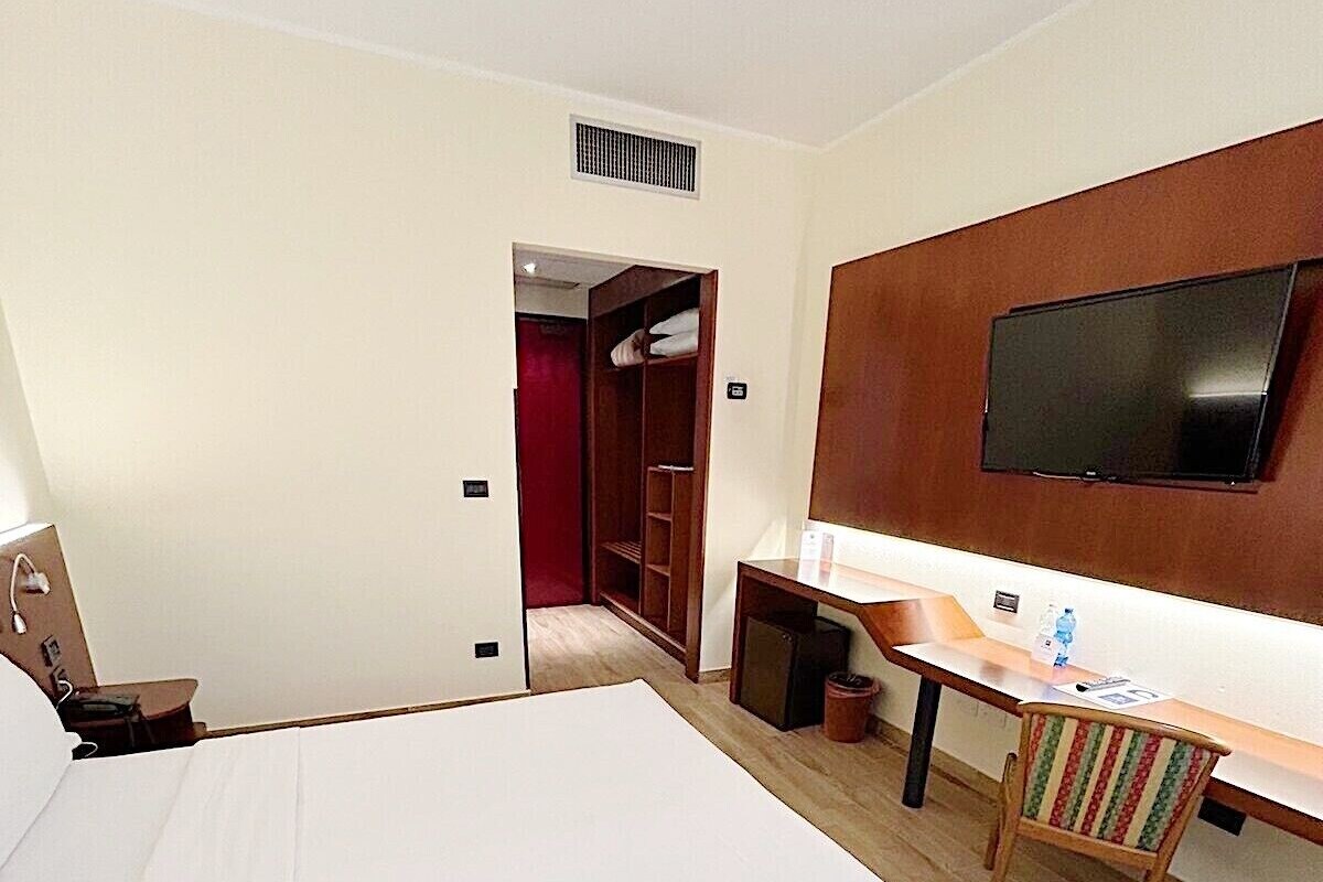 Habitación de hotel con una cama grande, un escritorio con silla, televisor y armario.