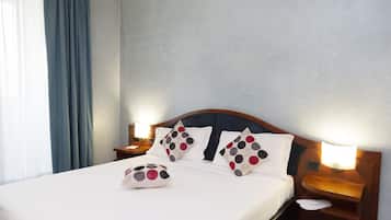 Un letto rifatto con lenzuola bianche e cuscini a pois, una testiera in legno e lampade sui comodini.