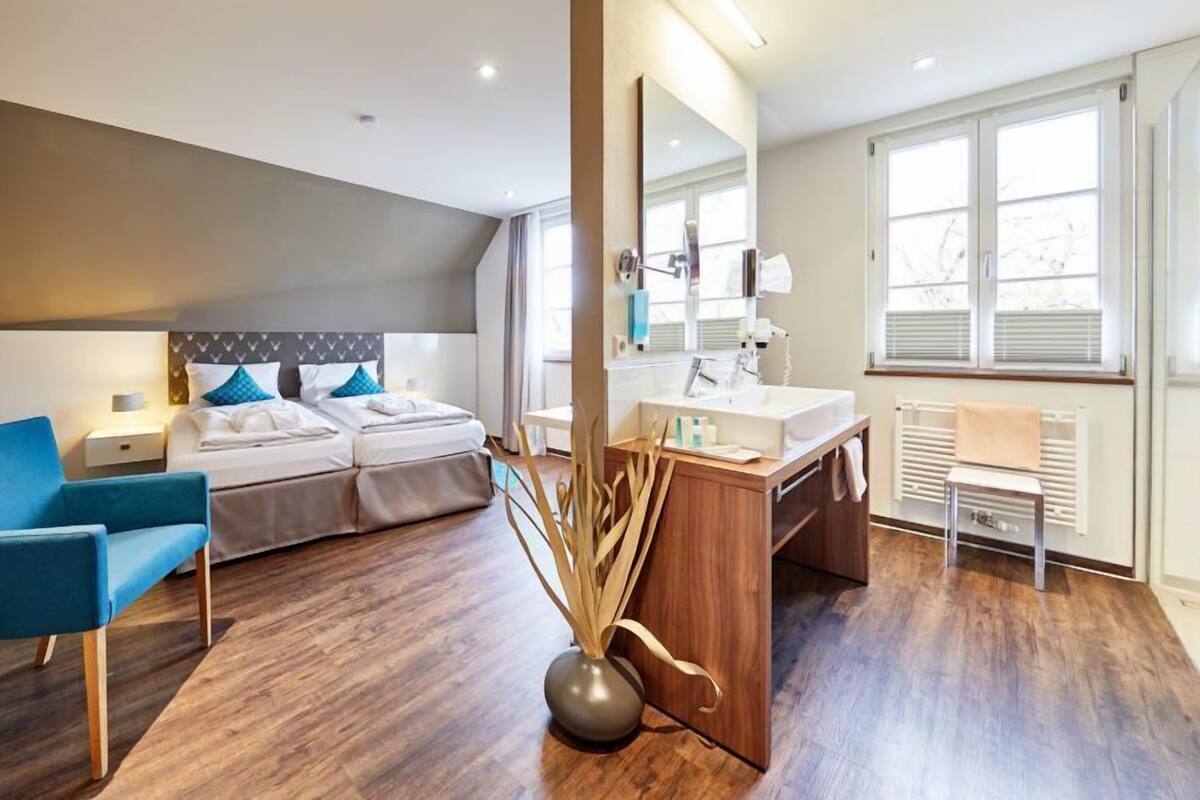 Una habitación de hotel moderna con una cama, un escritorio, una silla y un ventanal grande.