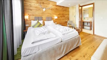 Ein modernes Hotelzimmer mit einem Holz-Kopfteil, einem großen Bett mit weißen Leinentüchern, einem kleinen Nachttisch mit Lampe und einem durchgehenden Türspalt sichtbaren Badezimmer.
