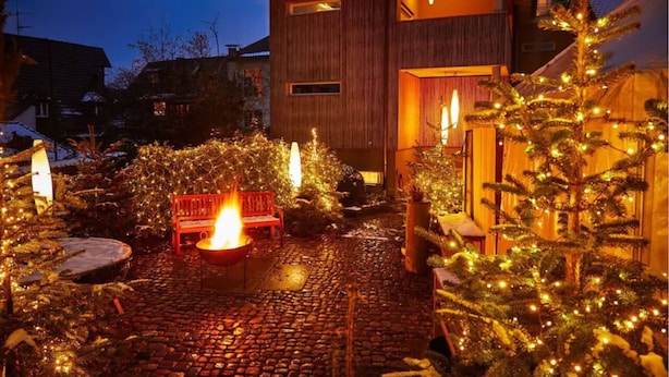 Un espacio exterior acogedor con un hogar, bancos y árboles de Navidad.