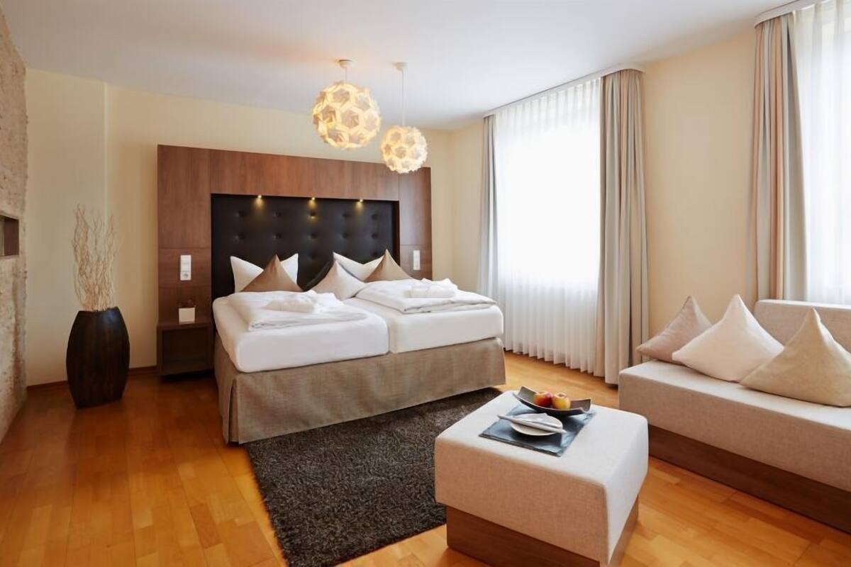 Una habitación de hotel moderna con una cama grande, un sofá, una mesa de centro y un jarrón decorativo.