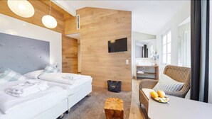 Una habitación de hotel moderna con una cama, una zona de estar con una mesa y sillas, un televisor montado en la pared y un baño visible a través de una puerta abierta.