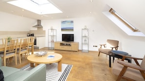 Ein modernes Wohnzimmer mit Essbereich, einem Fernseher und einem Schlafzimmer im oberen Bereich mit Dachfenster.