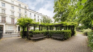 A paved courtyard with benches and a pergola covered in greenery, surrounded by buildings. - Imperial X (London)