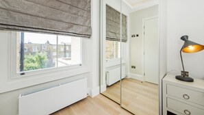 A room with a large window, a radiator, a mirror, a door, and a desk with a lamp. - Imperial X (London)