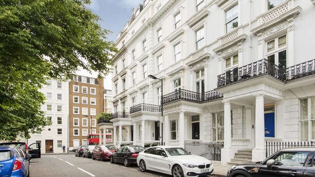 A row of white townhouses with balconies, parked cars, and a tree on the left. - Imperial X (London)