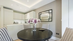 A modern dining area with a round table, striped chairs, a vase with flowers, and a kitchen in the background. - Imperial X (London)