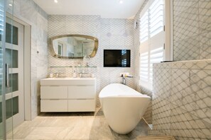 A modern bathroom with a freestanding bathtub, a large mirror, and a flat-screen TV mounted on the wall. - Immaculate Designer Home in Wandsworth (London)