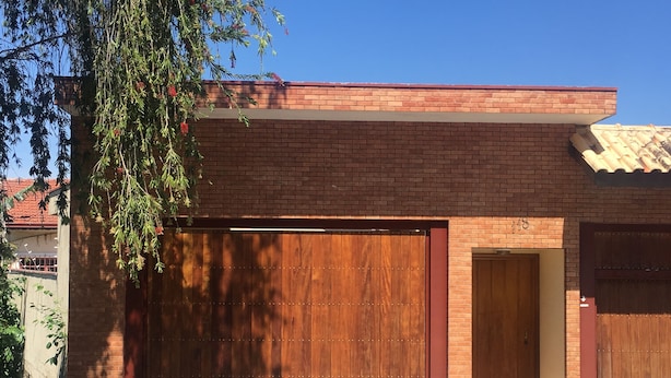 Un bâtiment moderne doté d’une grande porte de garage en bois, d’une façade en briques et d’une petite porte d’entrée.