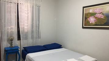 Ein Schlafzimmer mit einem Bett, einem Nachttisch, einer Lampe und einem Blumenbild an der Wand.