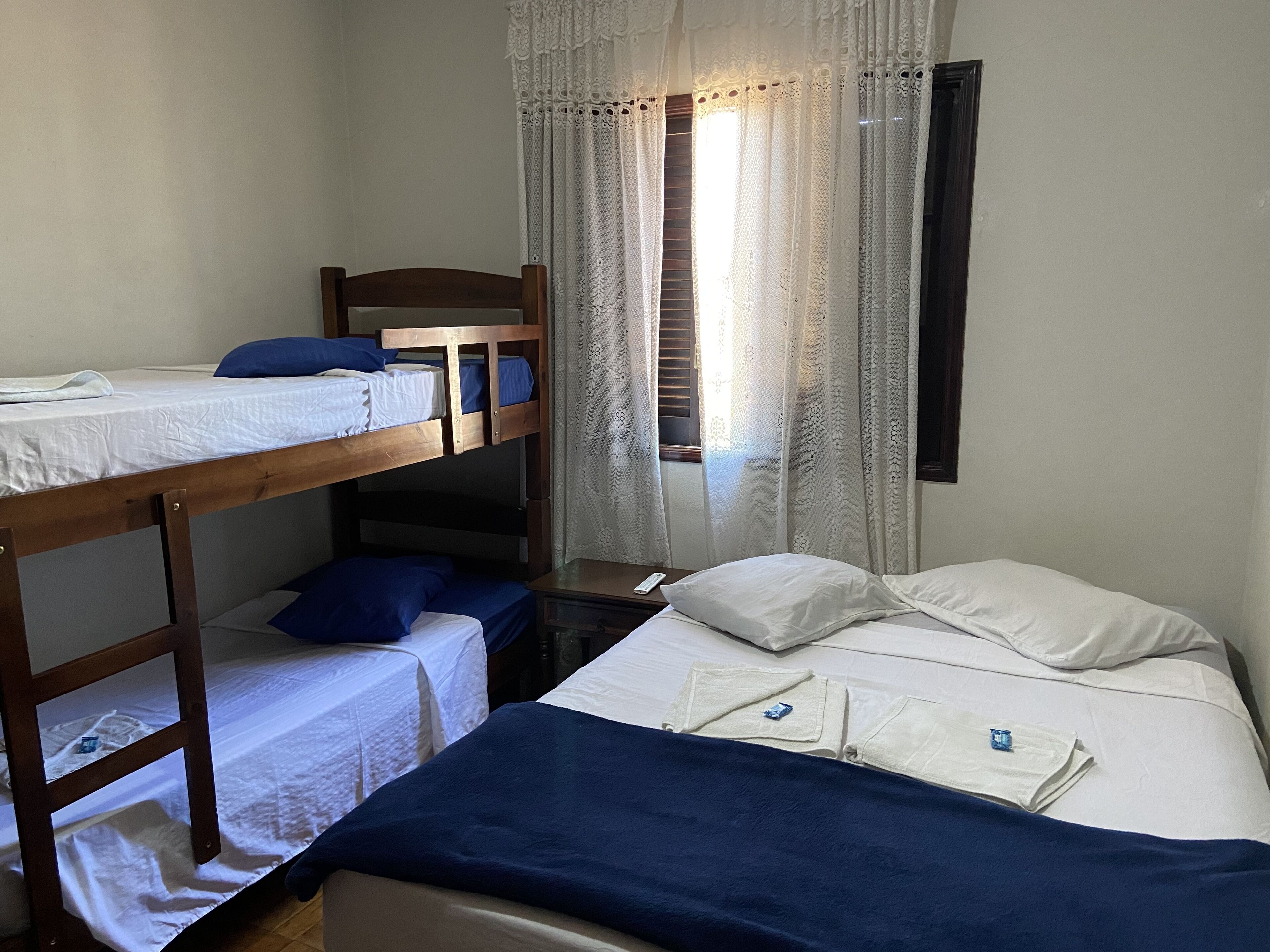 A bunk bed room with a window, white curtains, and a bedside table.